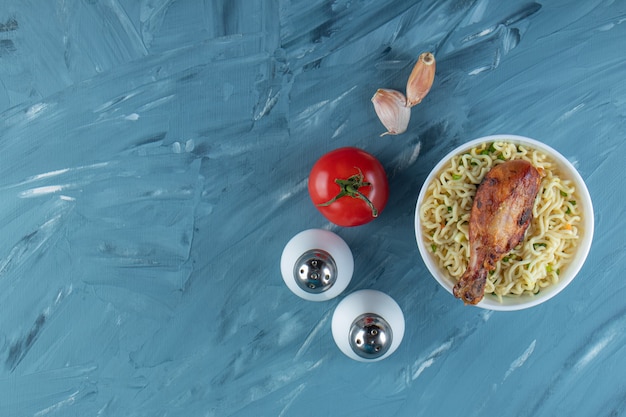 Hähnchenkeulen und Nudeln in einer Schüssel neben Salz, Tomaten und Knoblauch auf dem Marmorhintergrund.