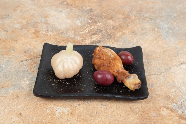 Hähnchenschenkel mit eingelegten Kornelkirschenbeeren und Knoblauch auf schwarzem Teller