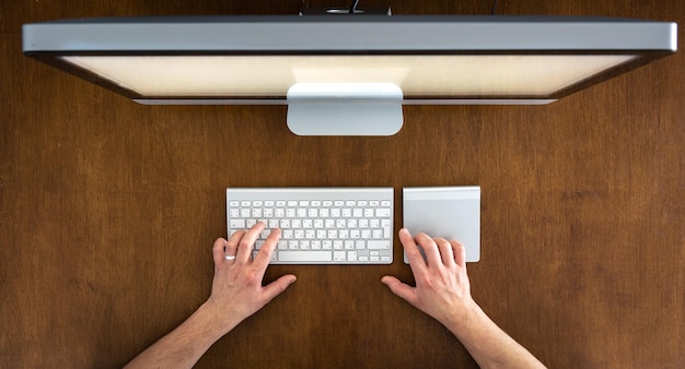 Hände benutzen einen Computer, während sie an der Tischplatte sitzen