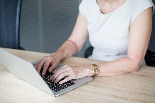 Hände der älteren geschäftsfrau tippen auf laptop