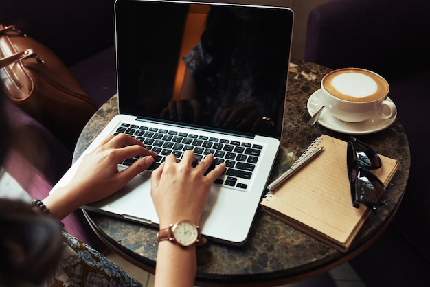 Hände der unerkennbaren frau, die auf laptop im café schreibt