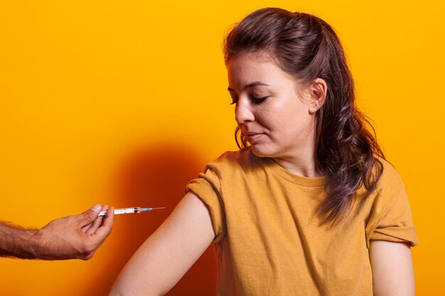 Hände des Arztes mit Spritze und Nadel, die Frau vor der Kamera impfen. Kaukasische Person, die die Injektion von Impfstoffen zum Schutz und zur Immunität gegen Coronavirus betrachtet. Erwachsene bei Impfung