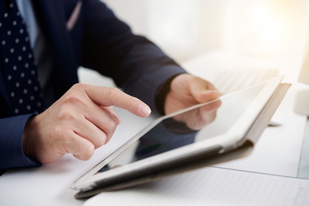 Hände des unerkennbaren Mannes im formalwear unter Verwendung der digitalen Tablette bei der Arbeit