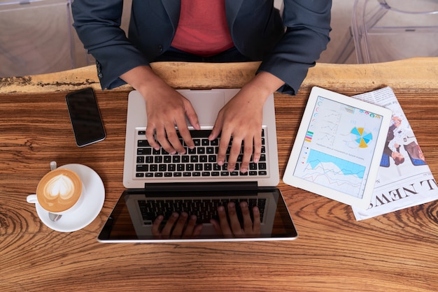 Hände des unerkennbaren Mannes sitzend am Holztisch im Café und an Laptop arbeitend