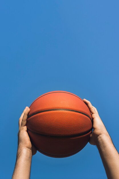 Hände, die Basketball auf blauem Himmel halten