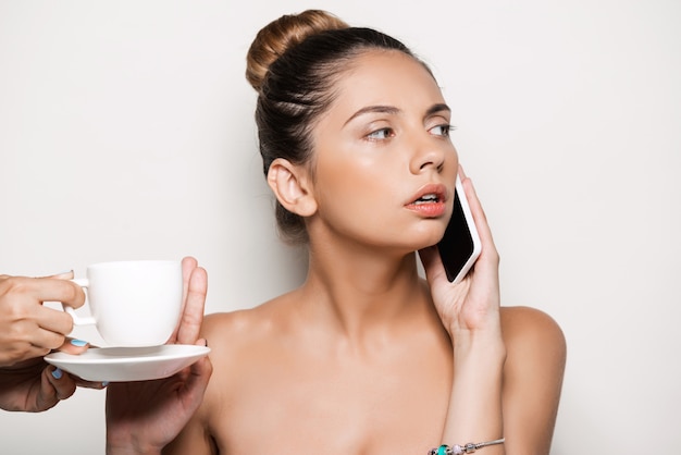 Hände, die der Frau, die am Telefon spricht, eine Tasse Kaffee anbieten