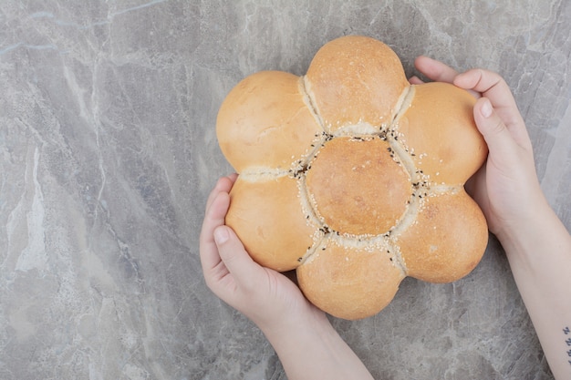 Hände, die ein rundes Brot auf Marmoroberfläche halten