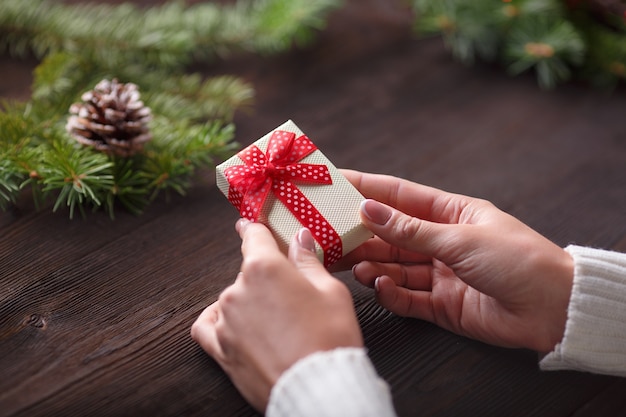 Hände, die eine Geschenk-Box mit einem dunklen Holztisch hält und einem Tannenzapfen