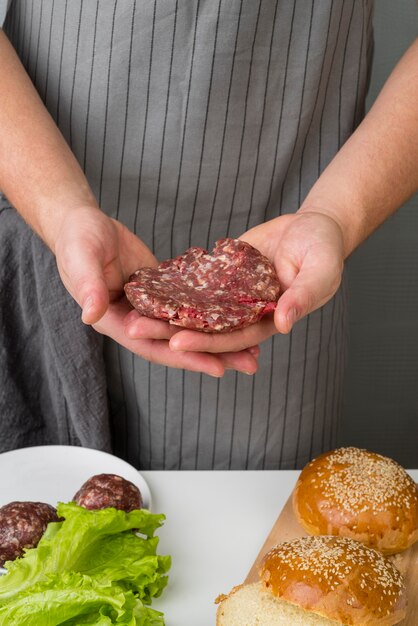 Hände, die Fleisch für Burger halten