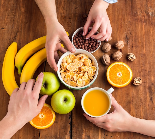 Hände, die gesundes hausgemachtes Frühstück des Müslis, der Äpfel, der frischen Früchte und der Walnüsse nehmen