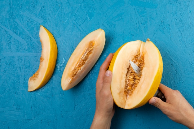 Hände, die Wassermelone auf blauem Hintergrund schneiden