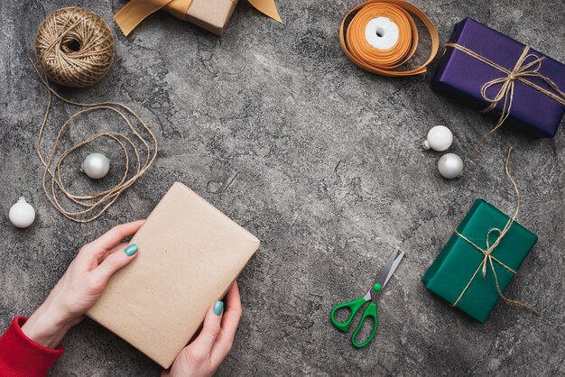 Hände, die Weihnachtsgeschenkbox mit Schnur und Sacissors halten