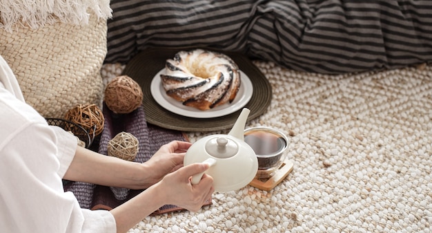 Hände einer jungen Frau gießen Tee aus einer Teekanne. Zubereitung des Frühstücks in gemütlicher Atmosphäre.