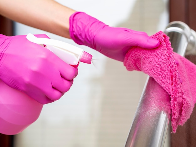 Hände mit OP-Handschuhen reinigen den Geländer mit einem Tuch und einer Waschung