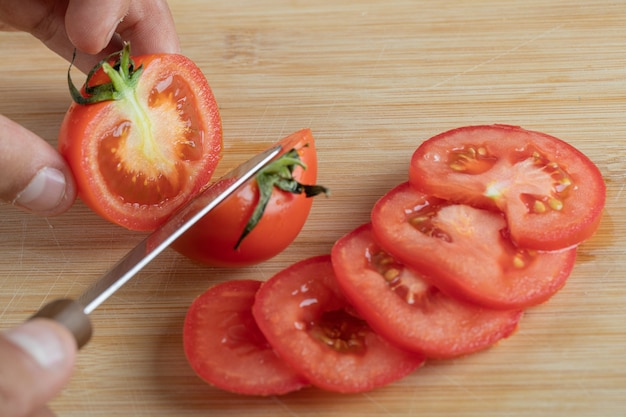 Hände schneiden eine frische Tomate auf einem Holztisch.