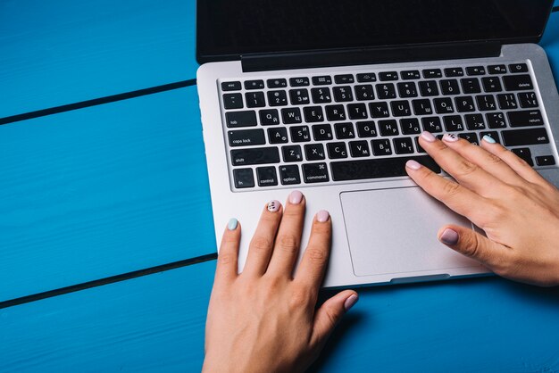 Hände unter Verwendung des Laptops auf blauem Schreibtisch