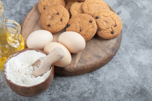 Haferflockenkekse mit Schokoladentropfen auf einem Holzbrett mit Zutaten herum