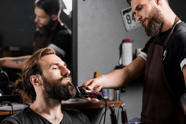 Hairstylist, der das Haar des männlichen Kunden mit elektrischem Trimmer trimmt