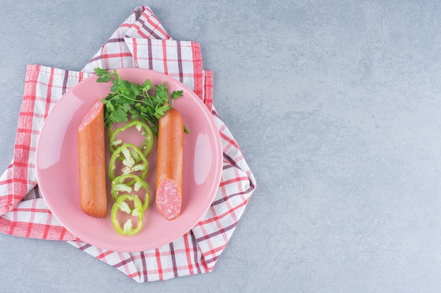 Halb geschnittene frische Salami mit Gemüse auf rosa Teller.