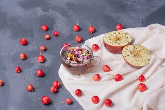 Halb geschnittenes Obst, Kirschen und ein Glas Saft mit Zitronenscheibe und Blumen auf Blau mit Tischdecke