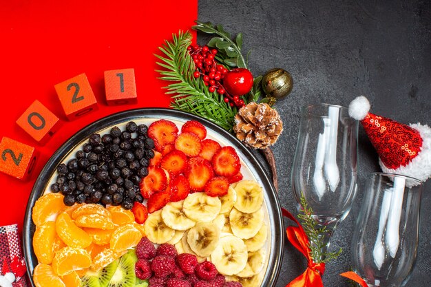 Halbe Aufnahme der Sammlung von frischen Früchten Weihnachtssocke Sant Laus Hut Zahlen Glaus Becher auf dunklem Hintergrund