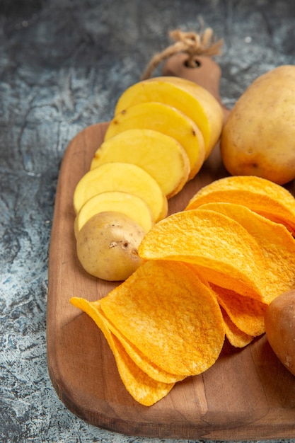 Halbe Aufnahme von knusprigen Pommes und ungekochten Kartoffeln auf Holzschneidebrett auf grauem Tischmaterial