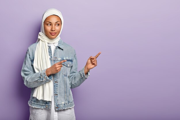 Halbe Länge Aufnahme der schönen arabischen Frau zeigt seitwärts, schlägt versuchen, App-Produkt, versucht weißen Schleier, Stylsih Jeansjacke