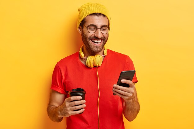 Halbe Länge Aufnahme von positiven Kerl lächelt auf dem Bildschirm des Smartphones, hat Online-Konversation im Chat, vergisst alle Probleme