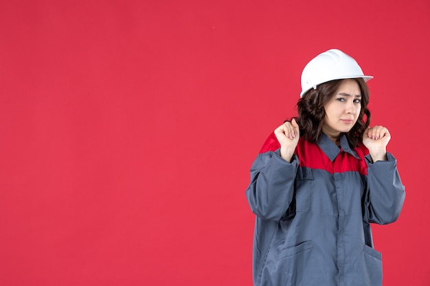 Halber Körperschuss einer überraschten Baumeisterin in Uniform mit Schutzhelm auf isoliertem rotem Hintergrund