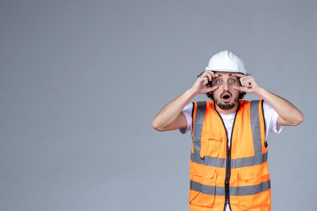 Halber Körperschuss von Shocke männlicher Architekt in Warnweste mit Schutzhelm über grauer Wellenwand