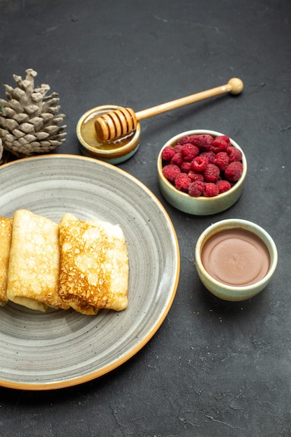 Halber Schuss des Abendessenhintergrundes mit köstlichem Pfannkuchenhonig und Schokoladenhimbeer- und Nadelbaumkegel auf schwarzem Hintergrund