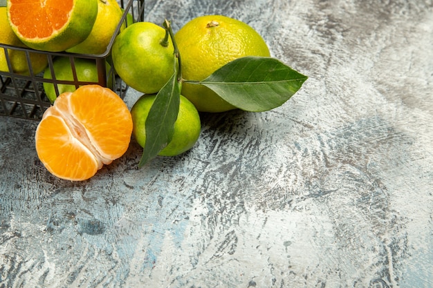 Halber Schuss eines Korbes voller frischer grüner Mandarinen und halbierter Mandarine auf grauem Hintergrund