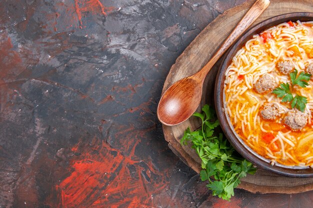 Halber Schuss köstliche Nudelsuppe mit Hühnchen auf Holzbrett Grünlöffel auf dunklem Hintergrund