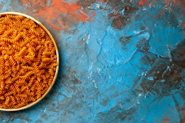 Halber Schuss roher italienischer Pasta in einer weißen Schüssel auf der rechten Seite auf blauem Hintergrund