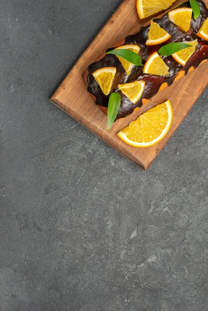 Halber Schuss von köstlichen Kuchen verziert mit Zitrone und Schokolade auf Schneidebrett auf schwarzem Tisch