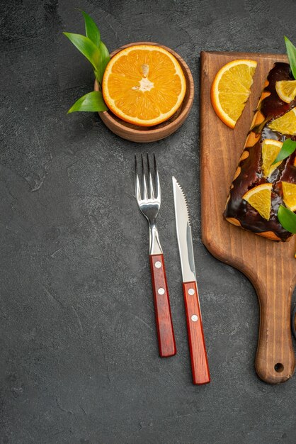 Halber Schuss von weichen Kuchen an Bord und geschnittene Zitronen mit Blättern auf dunklem Tisch