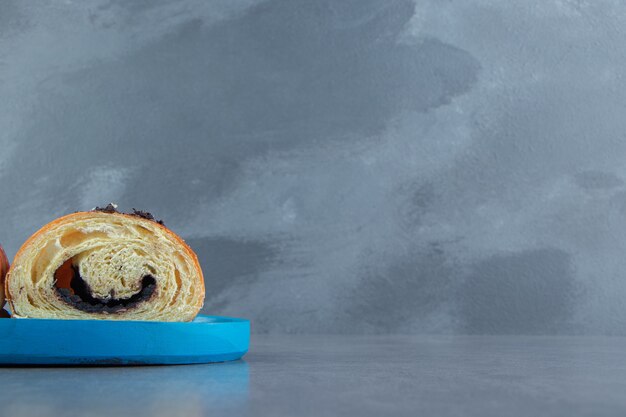 Halbgeschnittenes leckeres Croissant mit Schokolade auf blauem Teller.