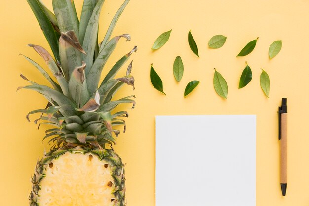 Halbierte Ananas mit Blättern; Stift und Weißbuch auf gelbem Hintergrund