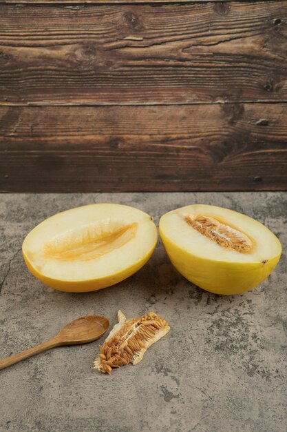 Halbierte köstliche gelbe Melonen auf Marmoroberfläche mit Holzlöffel beiseite.