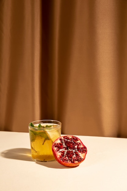 Halbierter Granatapfel mit köstlichem Cocktailgetränk vereinbarte auf Schreibtisch gegen braunen Vorhang