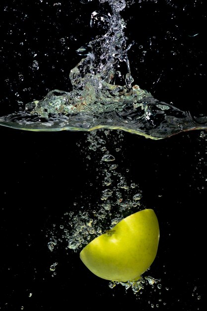 Halbierter grüner Apfel, der in Wasser mit Spritzen und Blase fällt