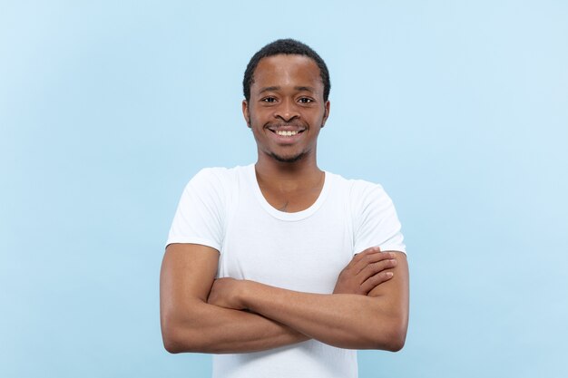 Halblanges Nahaufnahmeporträt des jungen Afroamerikaners im weißen Hemd auf blauem Raum
