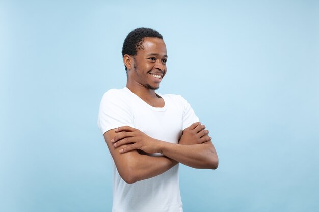Halblanges Nahaufnahmeporträt des jungen Afroamerikaners im weißen Hemd auf blauem Raum