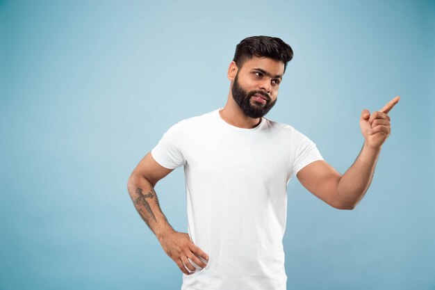 Halblanges Nahaufnahmeporträt des jungen Hindu-Mannes im weißen Hemd auf blauem Raum