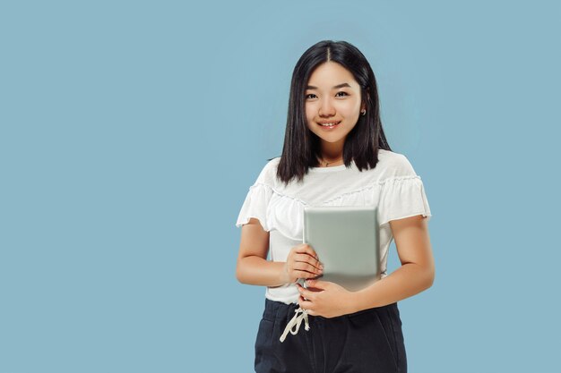 Halblanges Porträt der koreanischen jungen Frau. Weibliches Modell im weißen Hemd. Eine Tablette halten und lächeln. Konzept menschlicher Emotionen, Gesichtsausdruck. Vorderansicht.