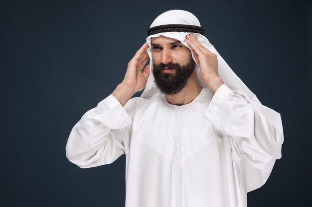 Halblanges Porträt des arabischen saudischen Geschäftsmannes auf dunkelblauem Studio