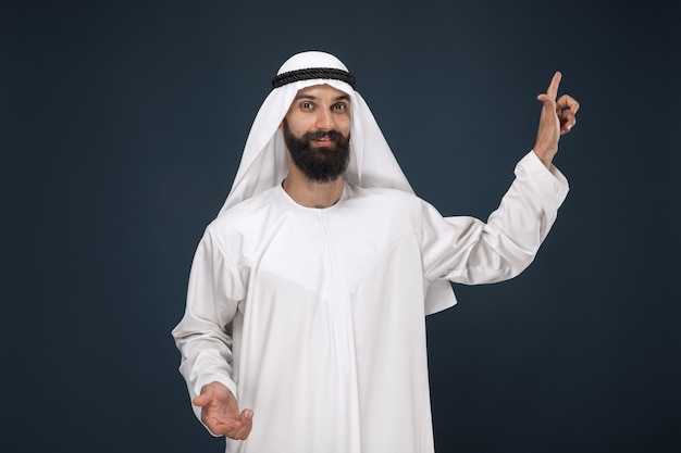 Halblanges porträt des arabischen saudischen mannes auf dunkelblauem studio