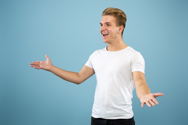 Halblanges Porträt des kaukasischen jungen Mannes auf blauem Studio