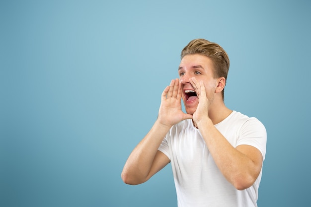 Halblanges Porträt des kaukasischen jungen Mannes auf blauem Studio