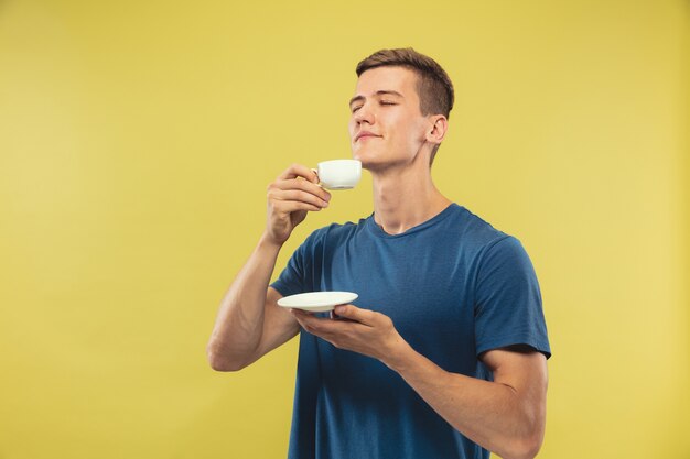 Halblanges Porträt des kaukasischen jungen Mannes auf gelbem Raum. Schönes männliches Modell im blauen Hemd